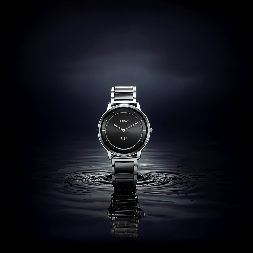 Titan Edge Fusion quartz analog black dial watch standing on reflective water with a ceramic strap.
